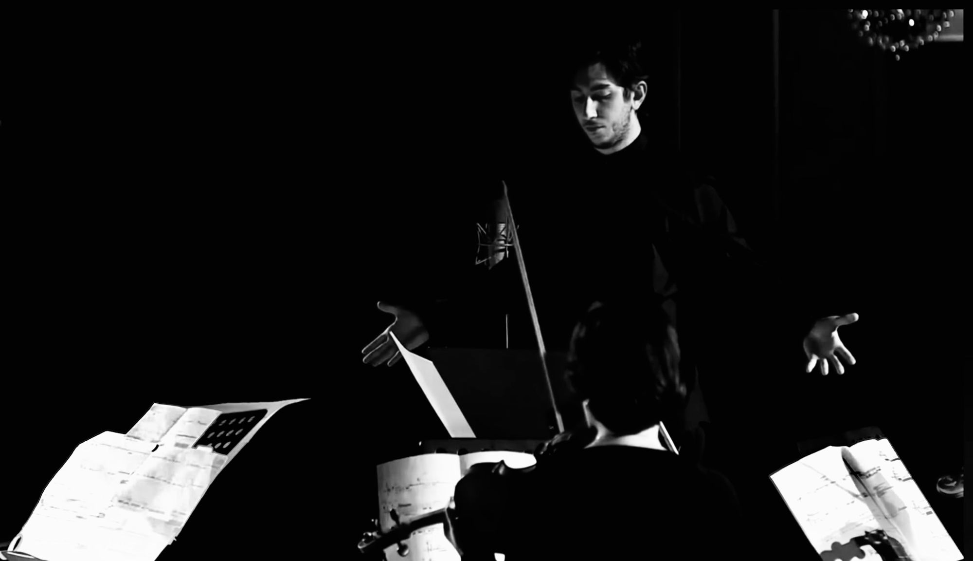 Gagi Sikharulashvili in rehearsal, standing over a string player and music stands in a dark hall